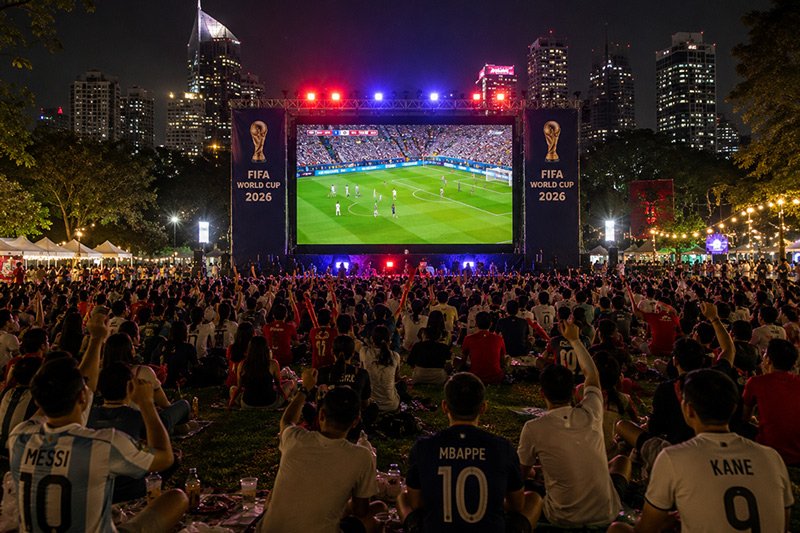 people in the crowd in the park watching football live on the big screen